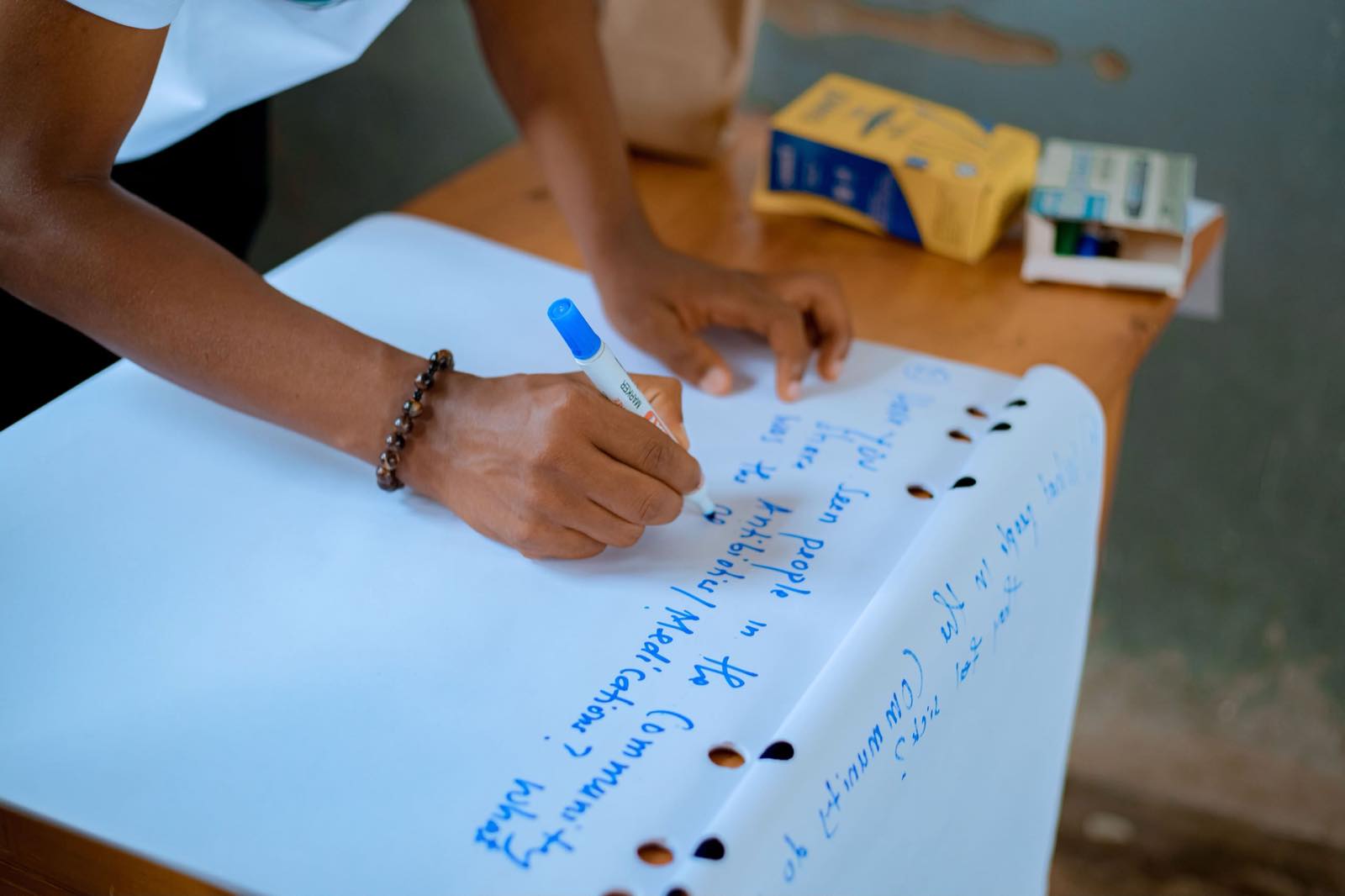 Close view of hands writing on a flip chart during a group discussion, with coloured sticky notes arranged across the page