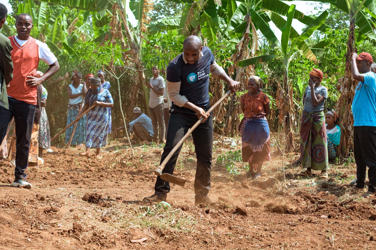 Community members and Zero AMR Initiative volunteers working the ground together with hoes during a community activity